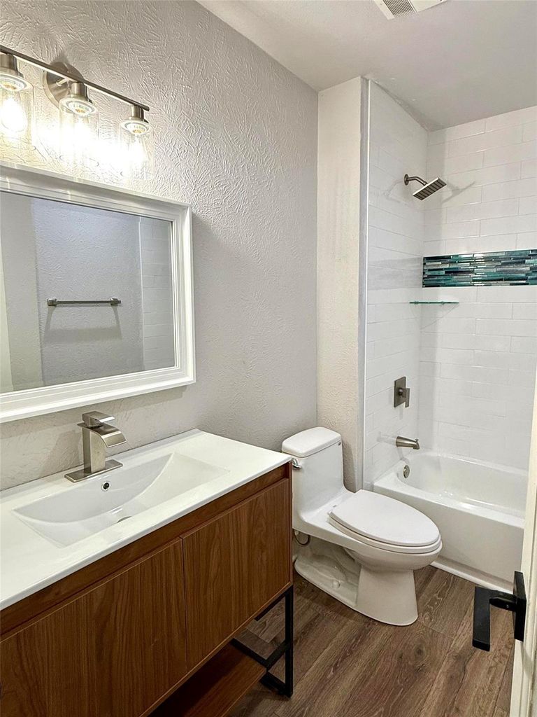 Bathroom featuring a textured wall, dark wood-style flooring, vanity, and  shower combination