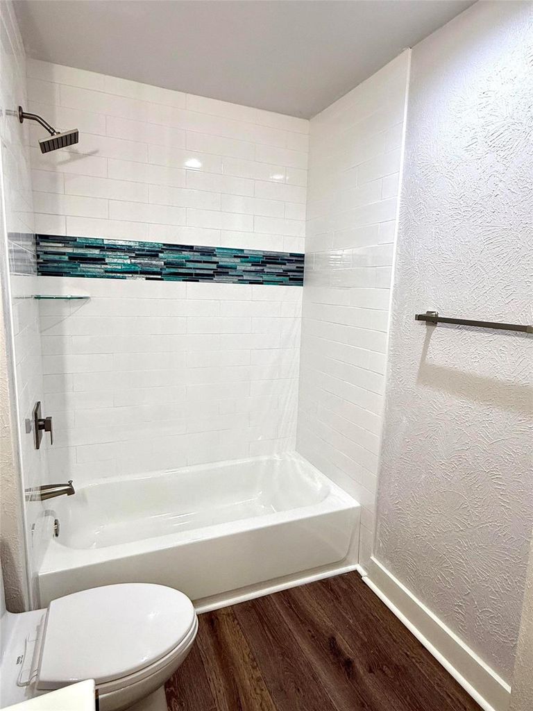 Bathroom with a textured wall, bathing tub / shower combination, and dark wood-type flooring