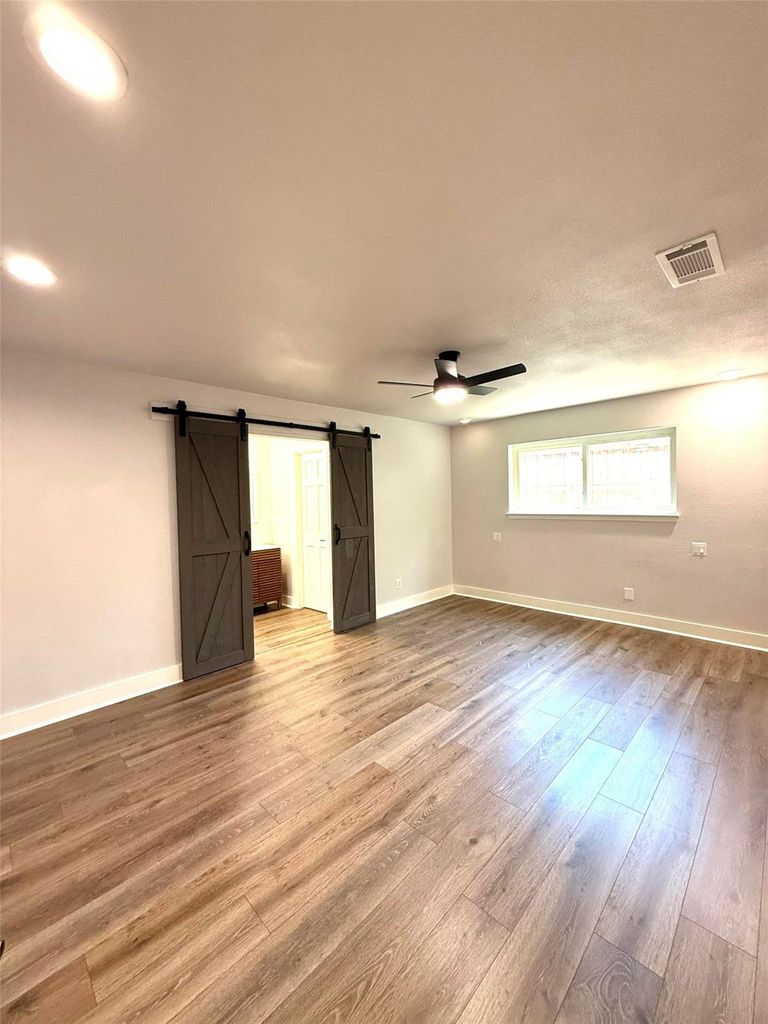 Empty room featuring a barn door, light wood finished floors, and ceiling fan