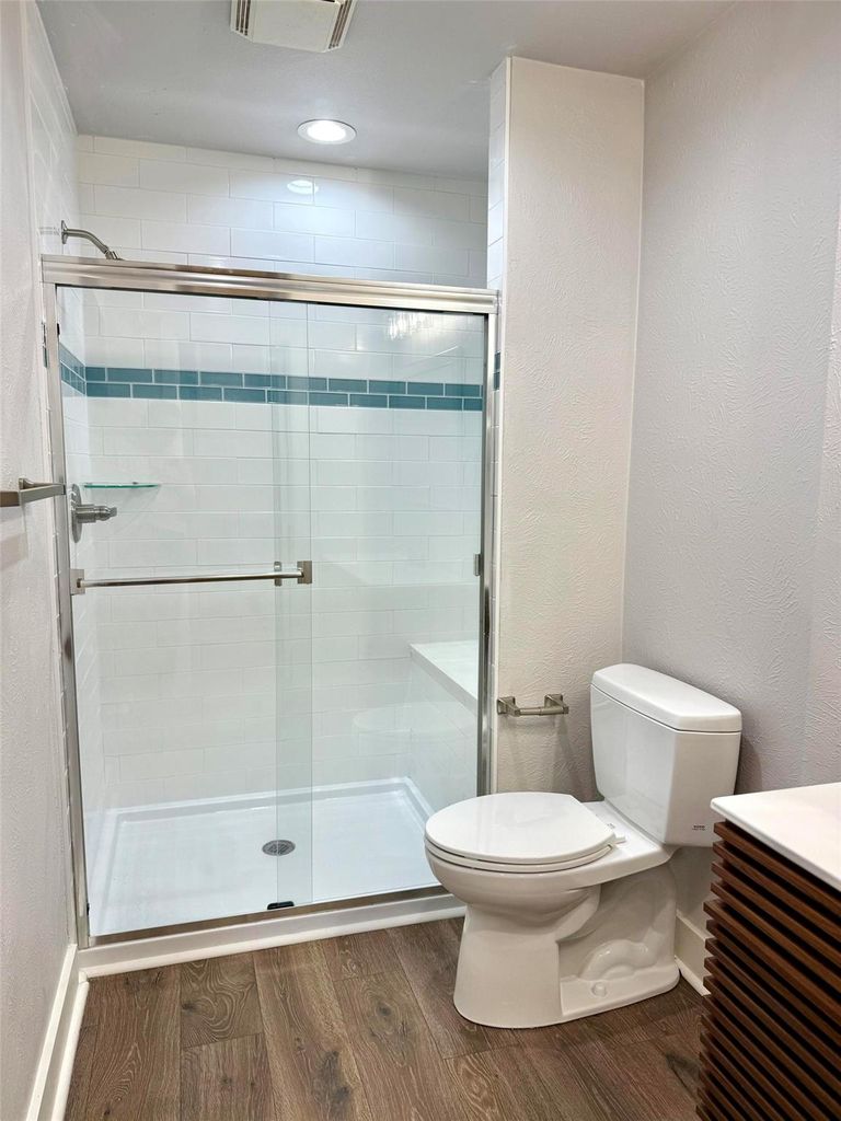 Full bath with vanity, a textured wall, a stall shower, dark wood-style flooring, and recessed lighting