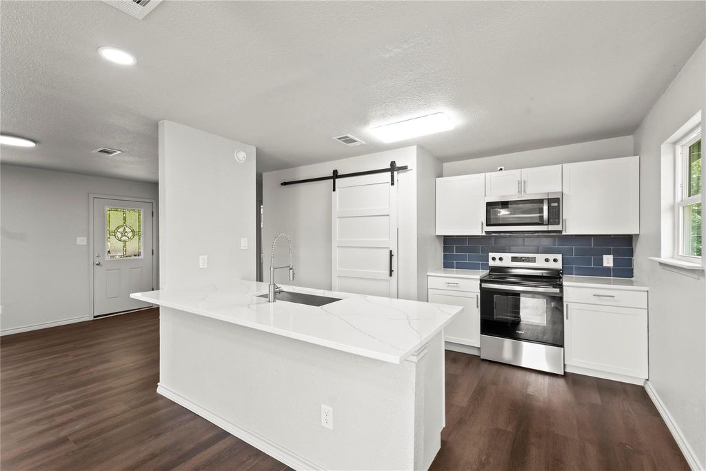 Kitchen featuring a barn door, stainless steel appliances, decorative backsplash, white cabinetry, and light stone counters