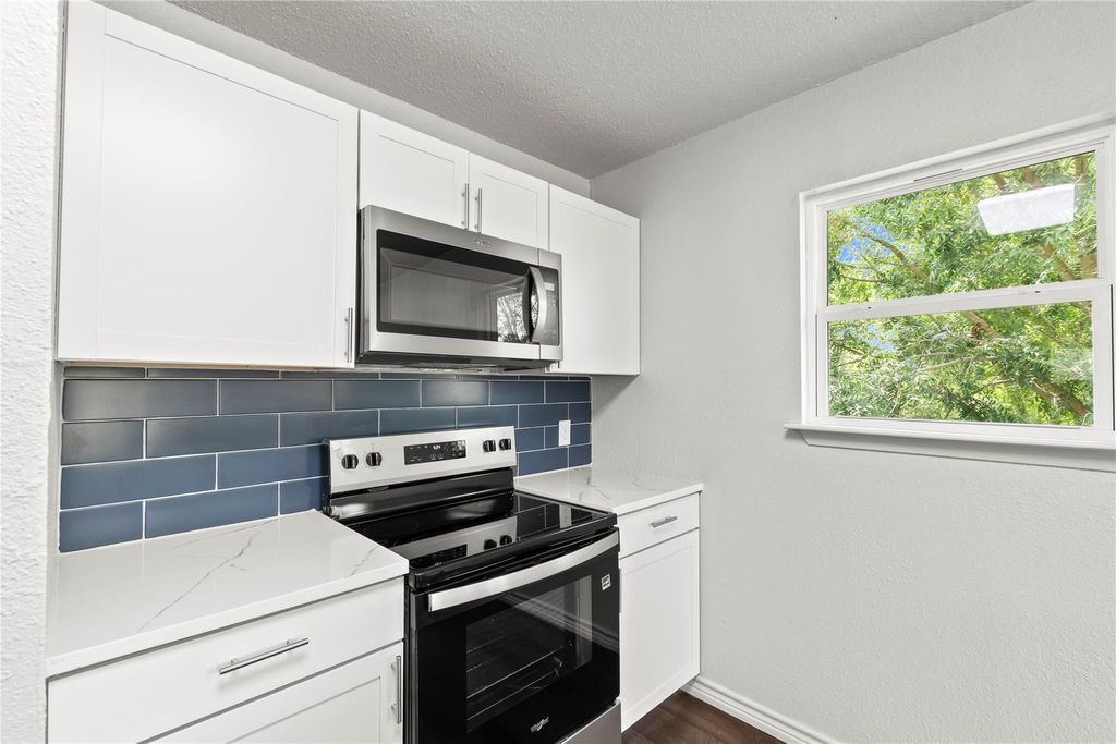 Kitchen featuring stainless steel appliances, decorative backsplash, white cabinetry, a textured ceiling, and light stone countertops
