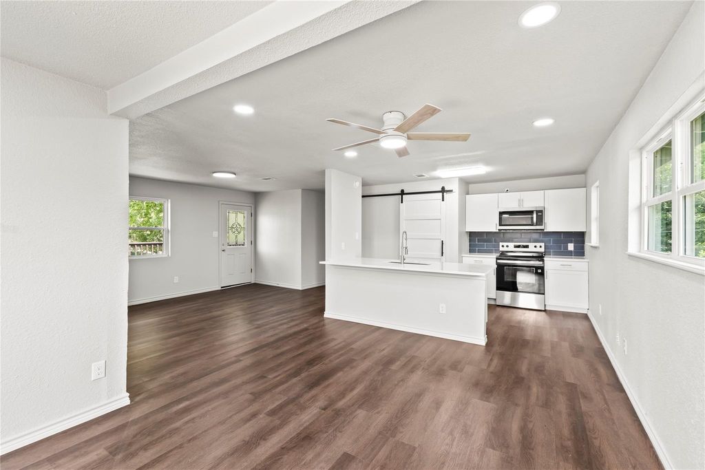 Unfurnished living room featuring a barn door, a ceiling fan, dark wood finished floors, healthy amount of natural light, and recessed lighting