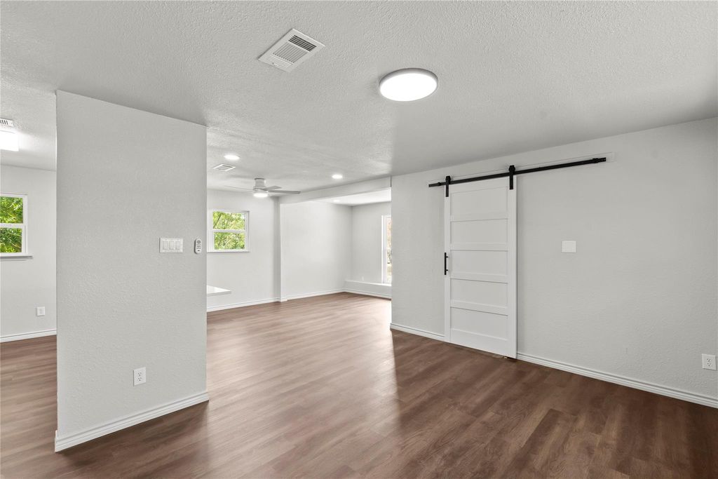 Unfurnished room with a barn door, dark wood-style floors, a textured ceiling, a ceiling fan, and recessed lighting