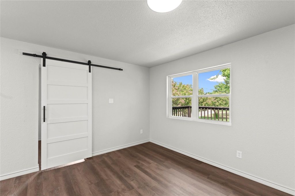 Spare room featuring a barn door, dark wood finished floors, and a textured ceiling