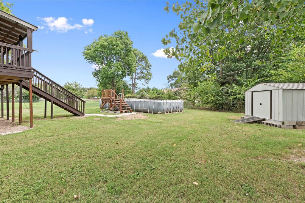 View of green lawn featuring stairs, a storage shed, and a wooden deck