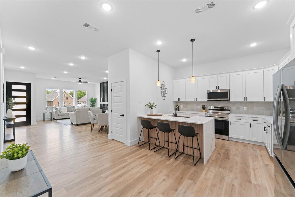 Kitchen featuring a kitchen breakfast bar, white cabinets, light stone countertops, decorative light fixtures, and stainless steel appliances