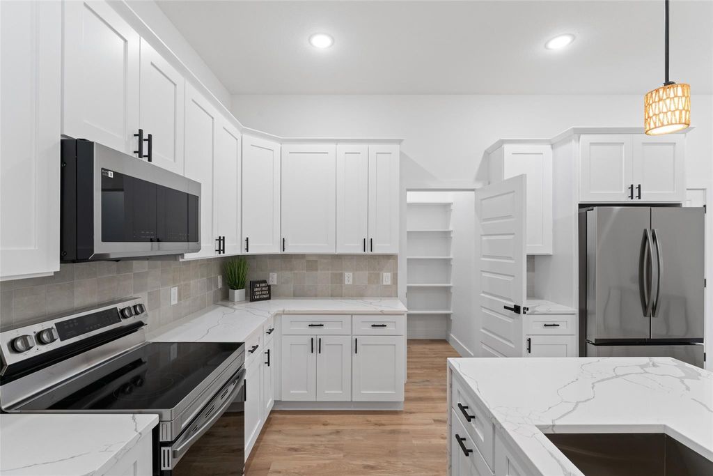 Kitchen with appliances with stainless steel finishes, white cabinets, light stone countertops, light wood-type flooring, and tasteful backsplash