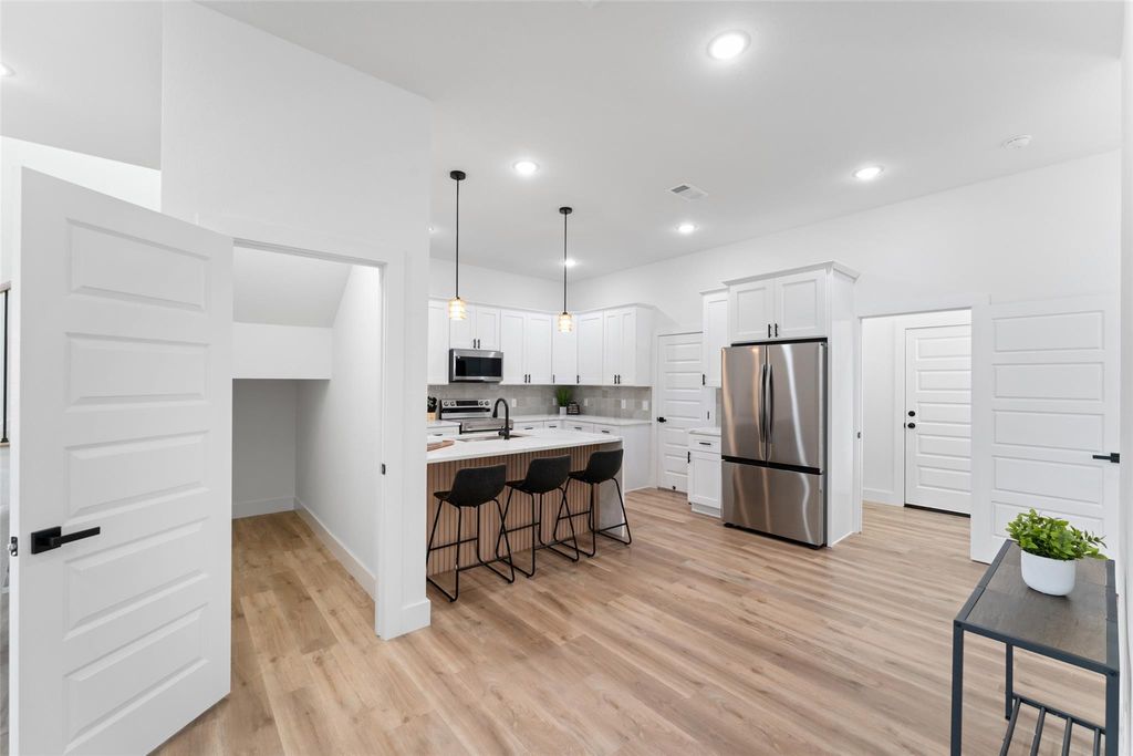 Kitchen featuring pendant lighting, a kitchen breakfast bar, stainless steel appliances, light wood finished floors, and an island with sink