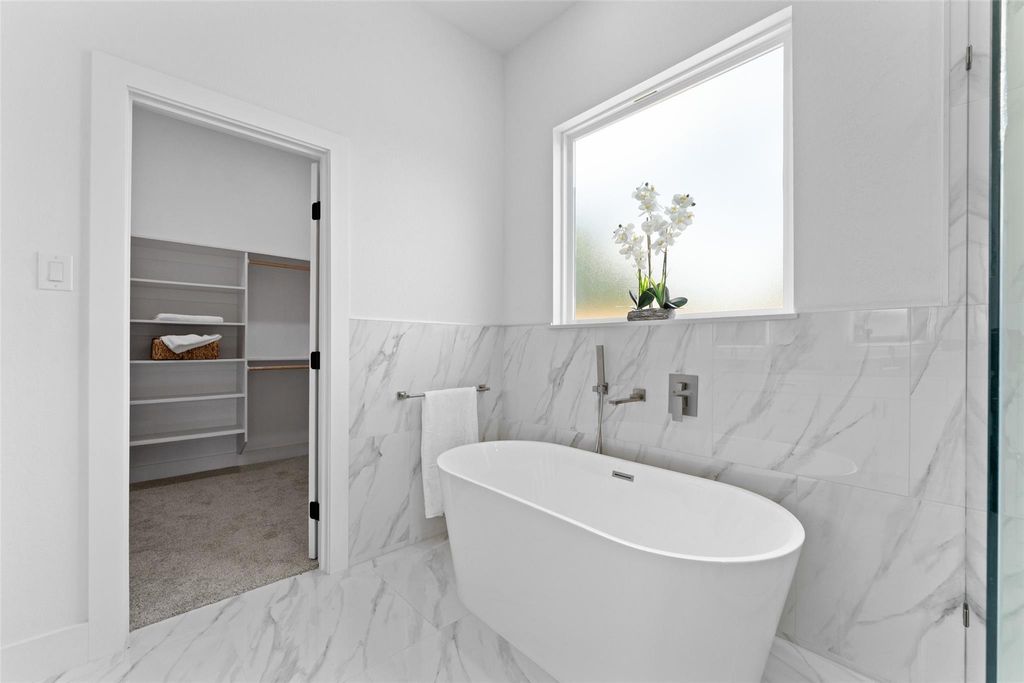 Full bath with a freestanding tub, a walk in closet, light marble finish floors, and tile walls