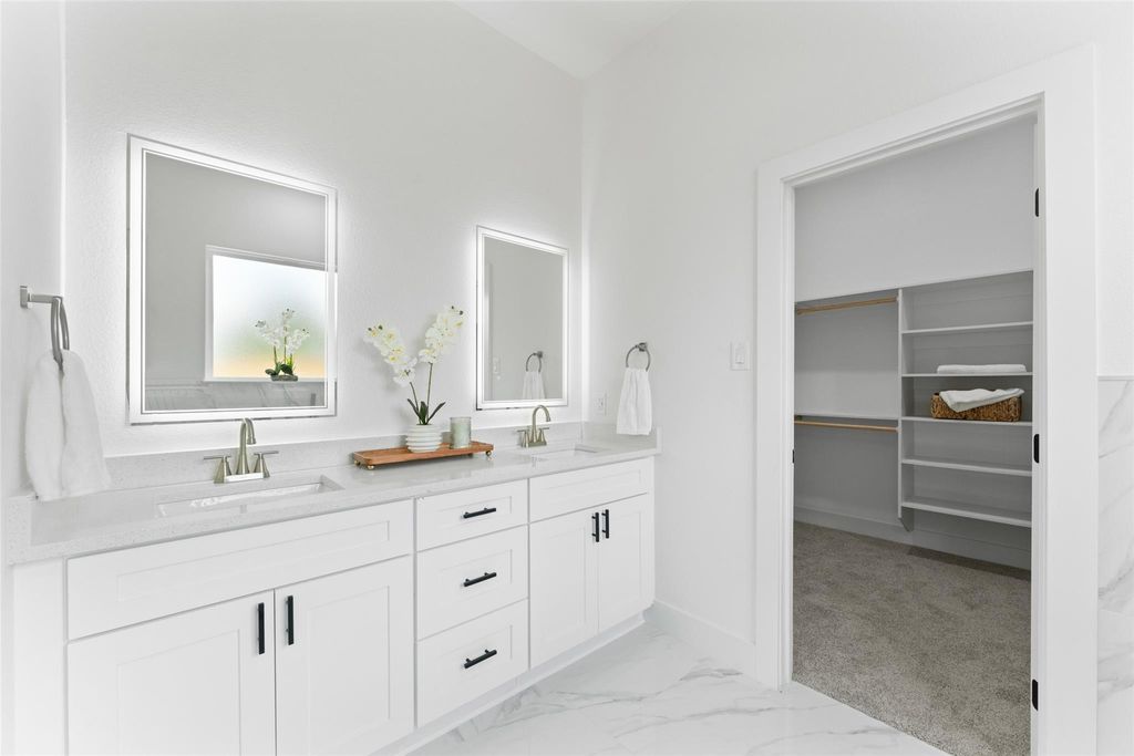 Full bathroom with double vanity, light marble finish floors, and a walk in closet