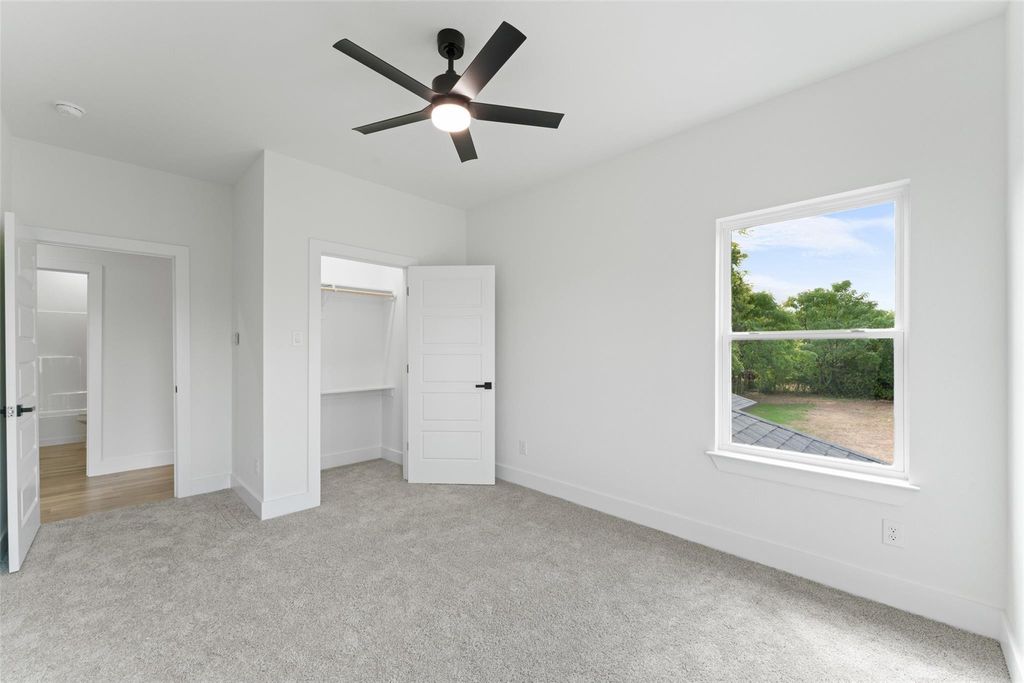 Unfurnished bedroom featuring light carpet, a spacious closet, and a ceiling fan