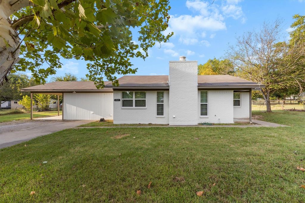 View of front of home featuring a chimney, a front lawn, brick siding, and a carport