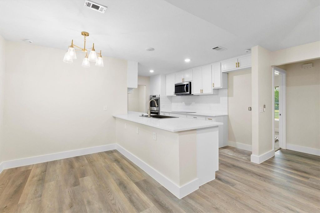Kitchen with backsplash, recessed lighting, white cabinetry, light wood-style floors, and light stone countertops