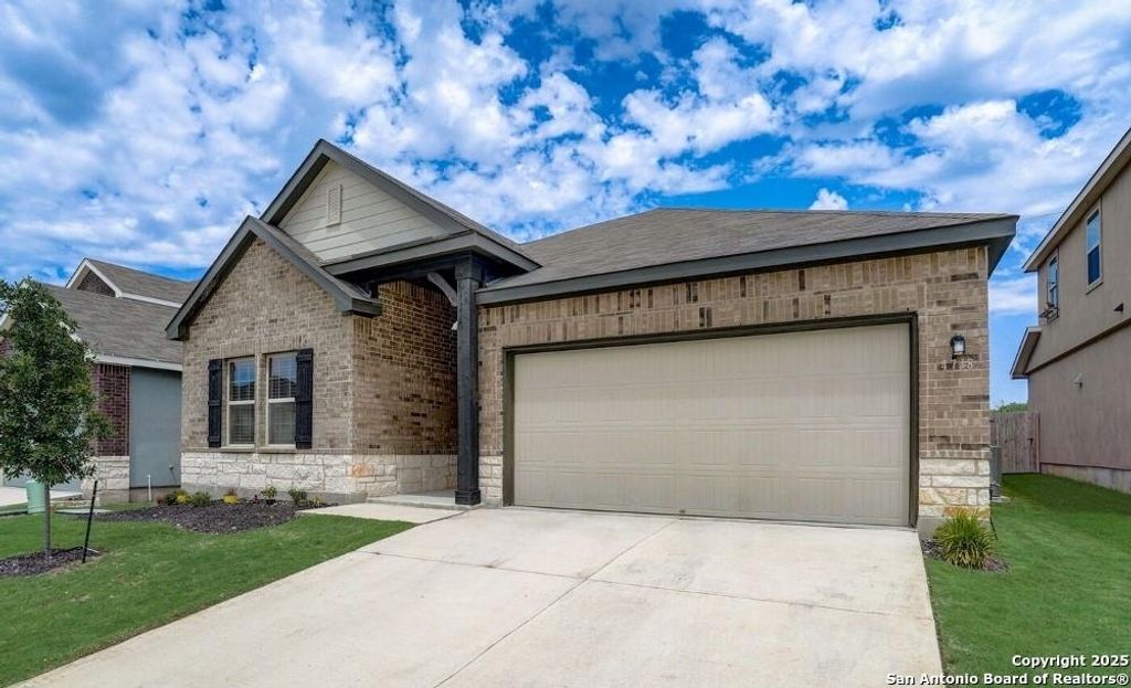 View of front of property with stone siding, an attached garage, driveway, brick siding, and a front lawn