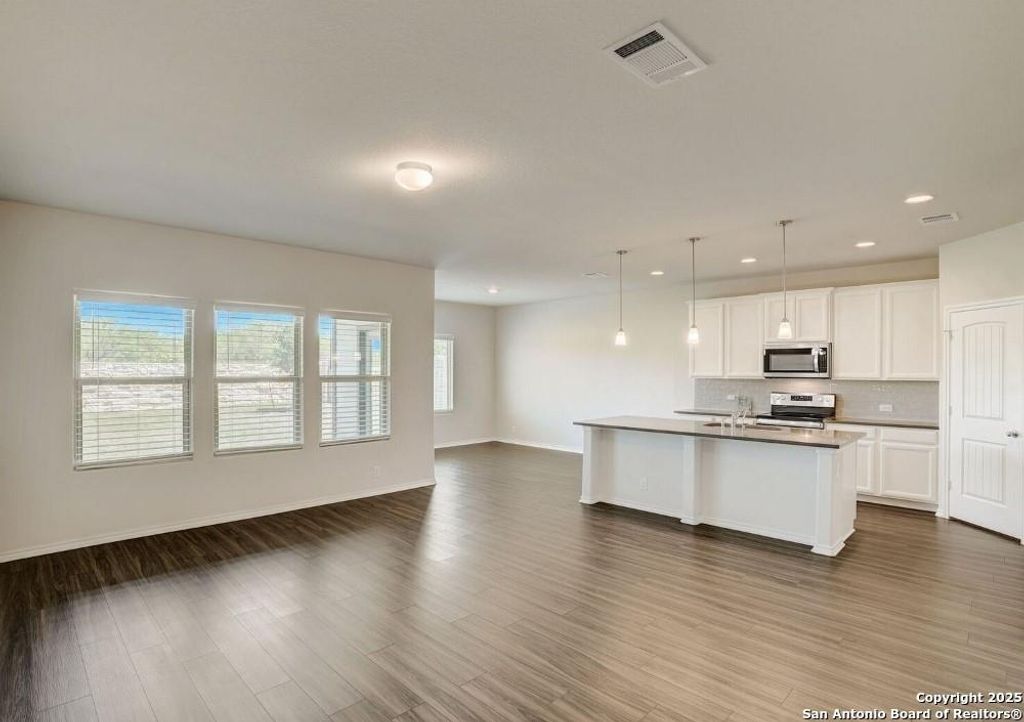 Kitchen featuring open floor plan, white cabinets, an island with sink, hanging light fixtures, and tasteful backsplash