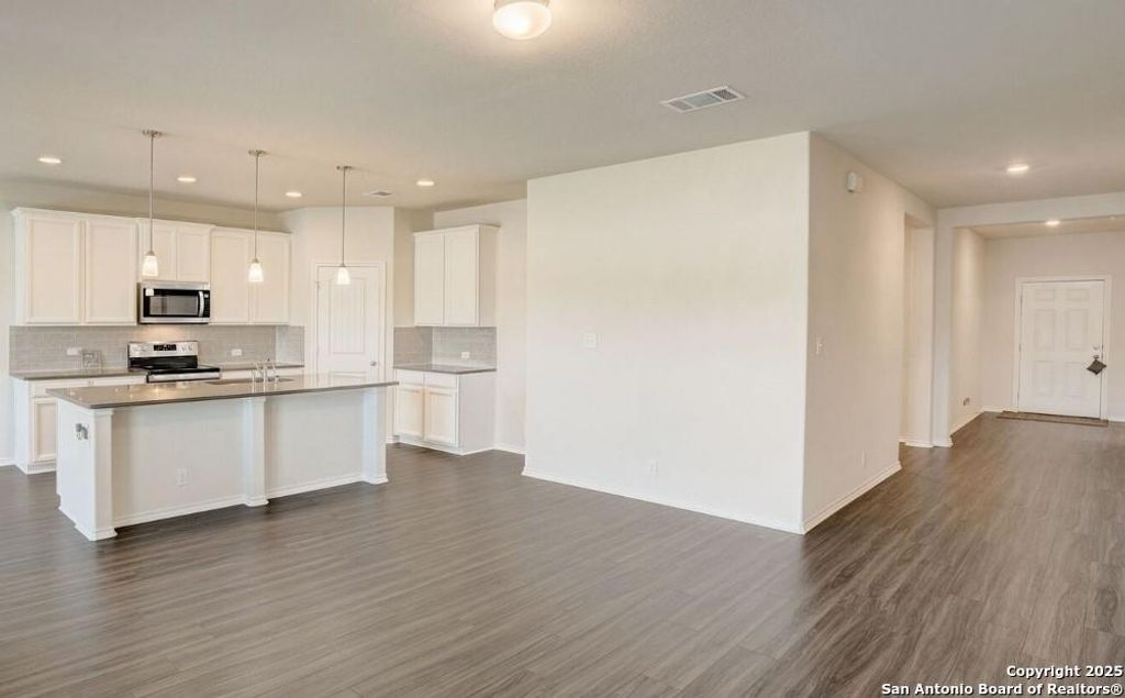 Kitchen featuring backsplash, white cabinets, dark wood-style floors, recessed lighting, and a kitchen island with sink