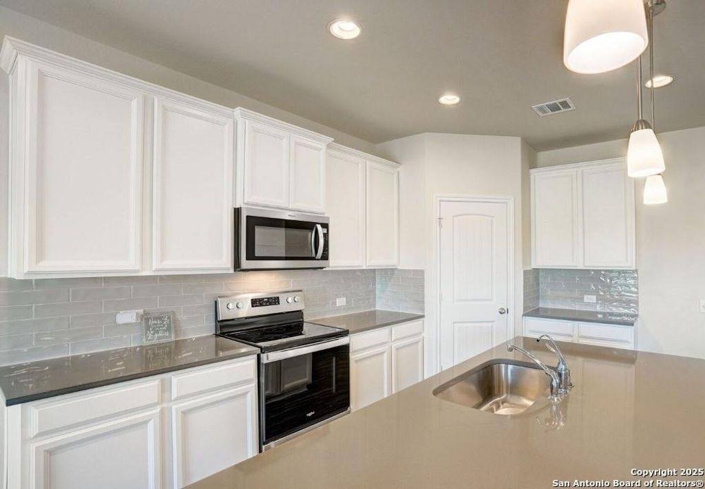 Kitchen featuring stainless steel appliances, decorative backsplash, decorative light fixtures, white cabinets, and recessed lighting