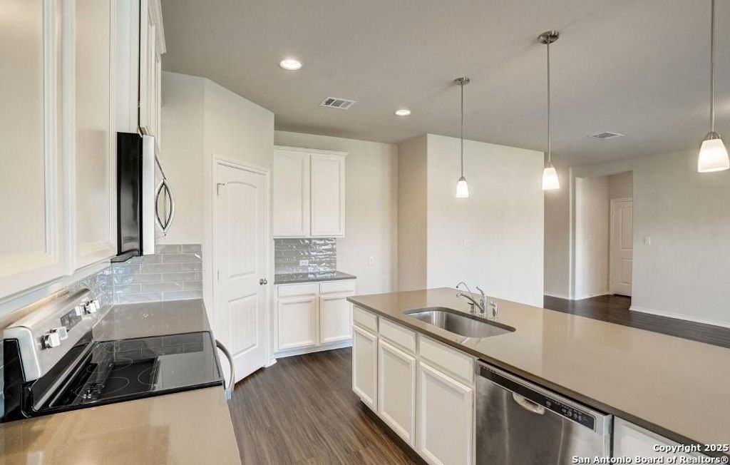 Kitchen featuring dark wood-style flooring, appliances with stainless steel finishes, white cabinetry, hanging light fixtures, and recessed lighting