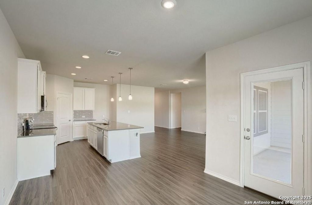 Kitchen with open floor plan, dark wood finished floors, decorative backsplash, white cabinets, and decorative light fixtures