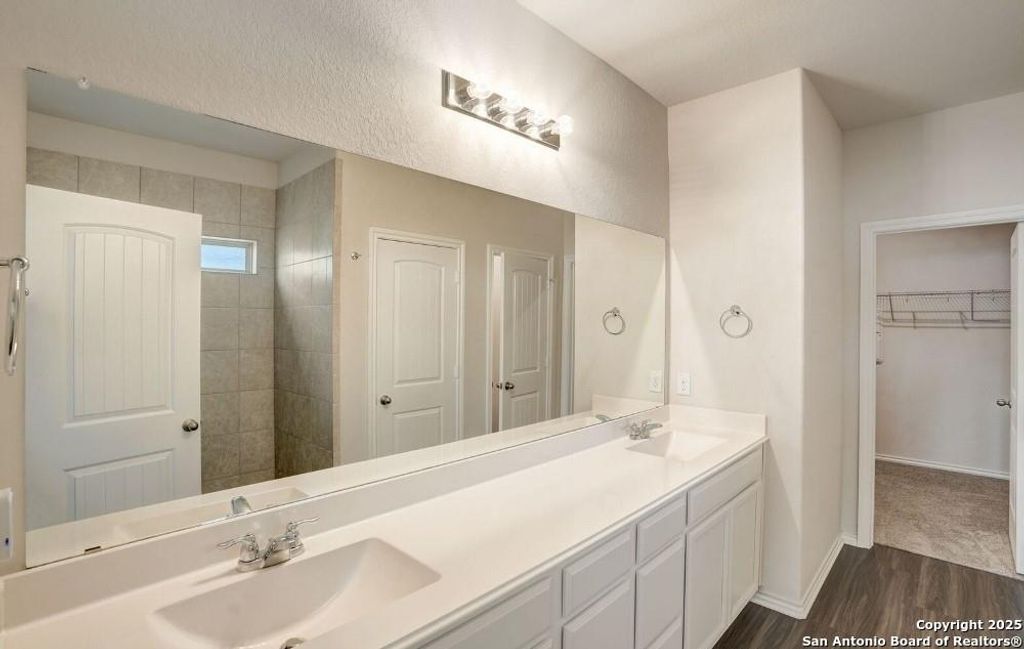 Bathroom with double vanity, a spacious closet, and dark wood-type flooring