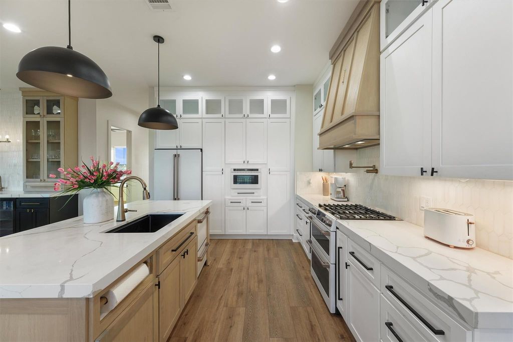 Chef’s kitchen with oversized quartz island, pendant lighting, custom cabinetry, and premium appliances.