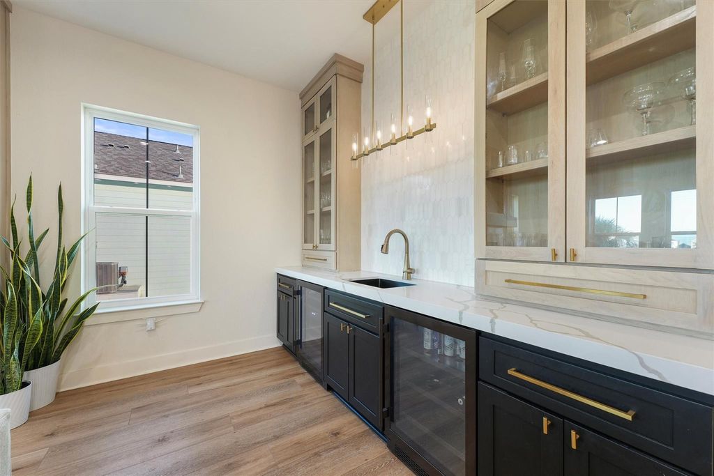 Stylish wet bar with marble backsplash, quartz counters, glass cabinetry, and brass fixtures.