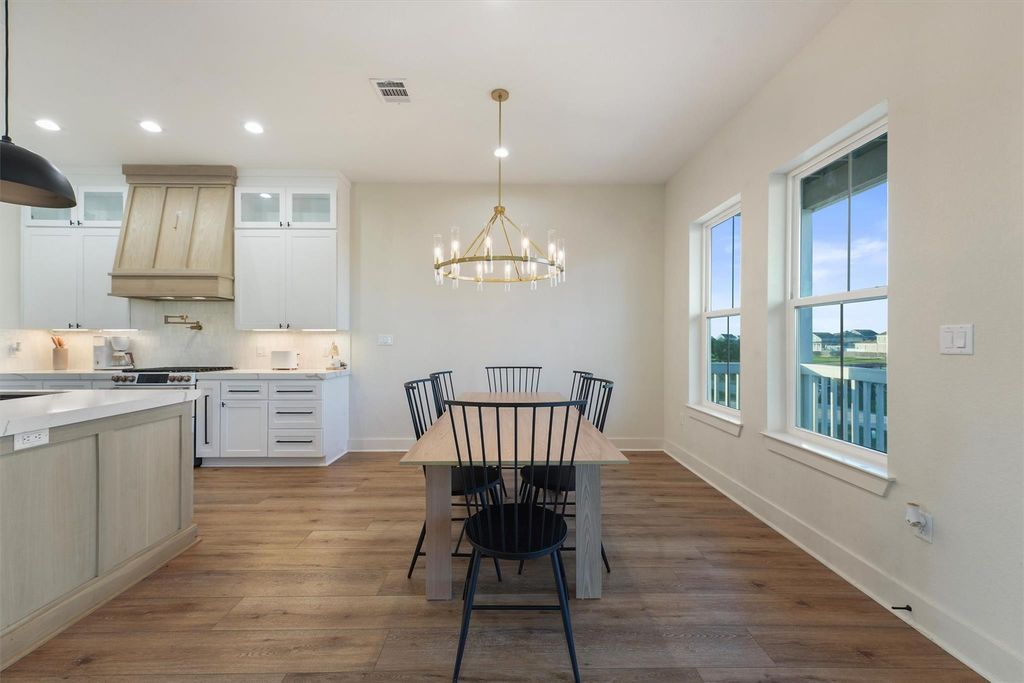 Open dining space with modern chandelier, hardwood floors, and large windows bringing in natural light. 