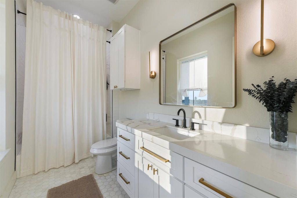 Stylish full bath with quartz countertop, gold accents, and ample cabinet storage. 