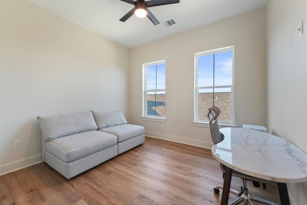 Bright secondary bedroom or office with hardwood floors, ceiling fan, and natural light.