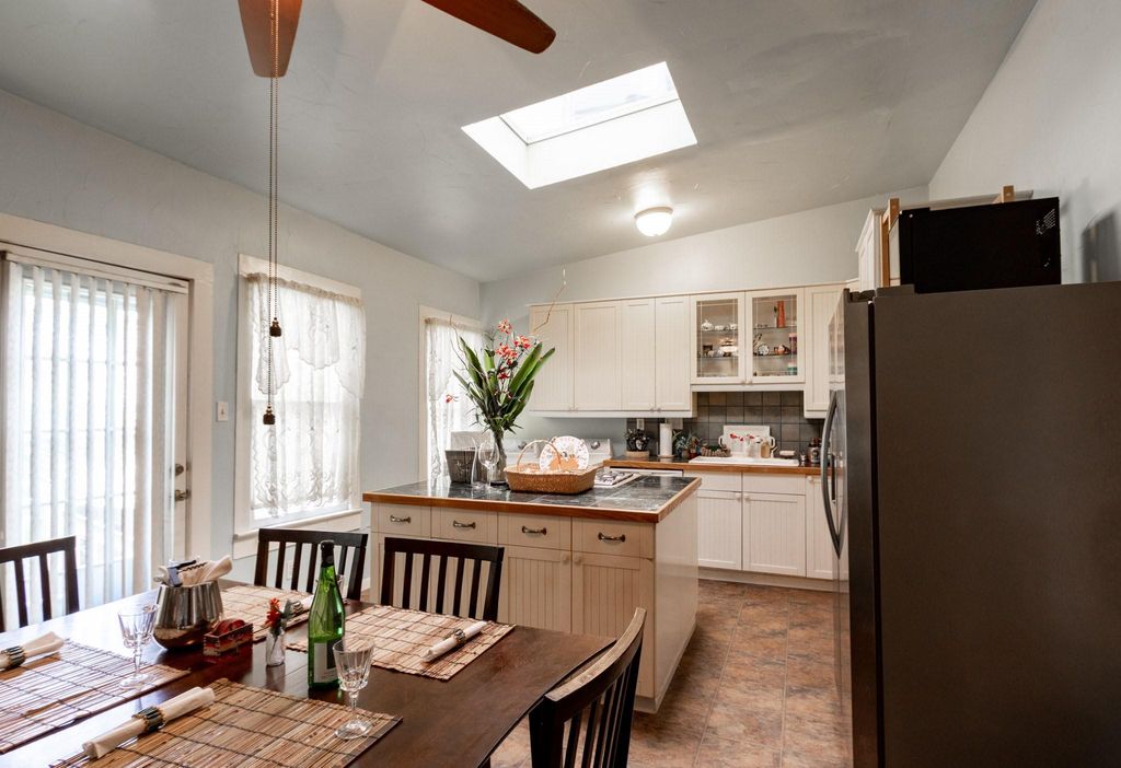 Looking from the living room doorway into the kitchen. Back door on the left. Kitchen island, with gas stove, in the background. Refrigerator to the right.  Table for six in the foreground. And, a skylight!