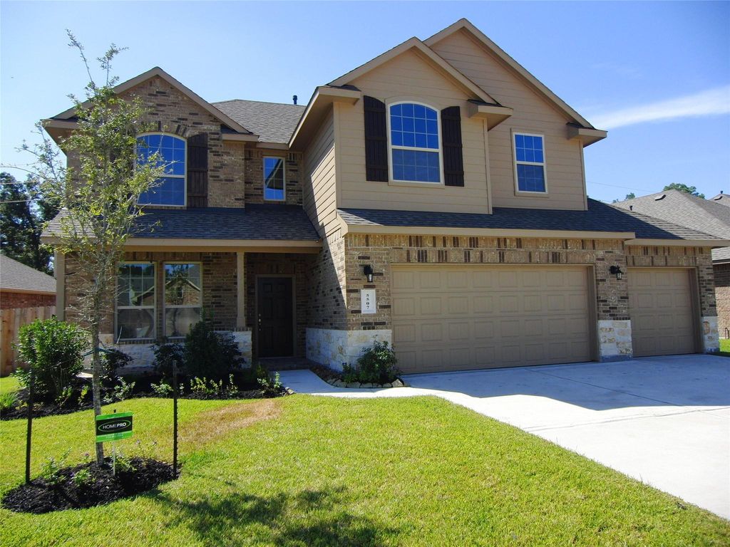 This two-story home features a classic brick facade with modern accents, large windows, and a three-car garage. The well-maintained front yard includes a small tree and fresh landscaping, adding to its curb appeal.