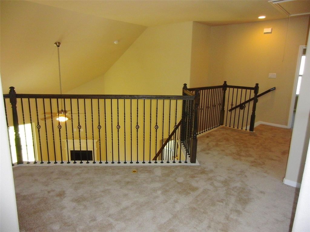 Carpeted landing area with decorative wrought iron railings overlooking a lower level. The space is well-lit and features a sloped ceiling, creating an open and airy feel.