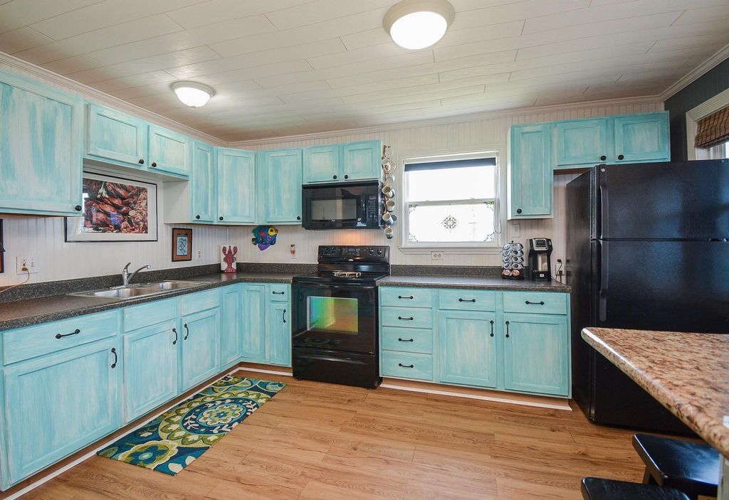 This kitchen features charming light blue cabinets, and black appliances.. It includes ample counter space, a double sink, and a window for natural light, creating a bright and inviting atmosphere.