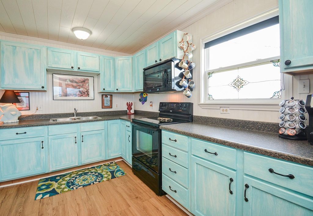 This bright kitchen features charming turquoise cabinets, a sleek black oven, and a large window with decorative glass. The space is accented by gorgeous flooring and modern countertops, offering a stylish cooking area.