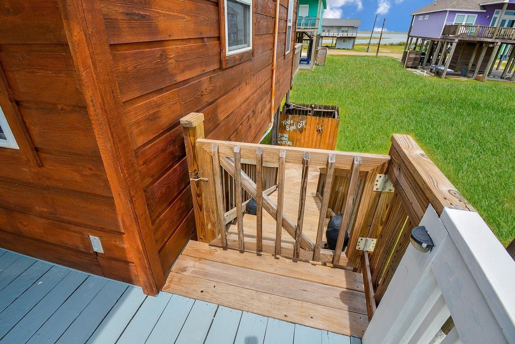 The stairs lead down to a grassy area, with views of nearby homes and a bay view in the background. The deck features a safety gate, adding a rustic charm to the outdoor space.