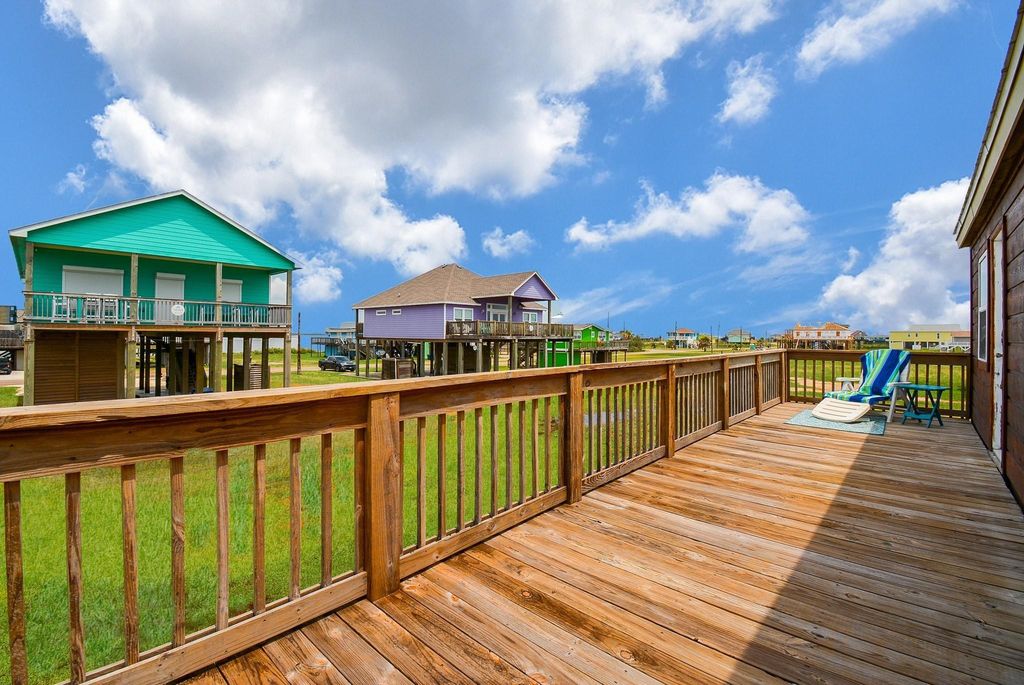 This photo showcases the back sun deck with a lounge chair and small table, perfect for relaxing. The area offers a clear view of a grassy landscape and neighboring houses, and bay views.