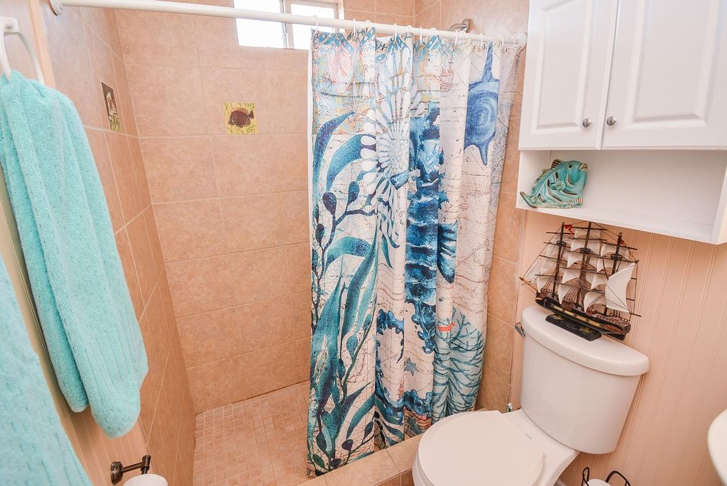 This bathroom features a tiled walk-in shower with a colorful ocean-themed curtain. It includes a white cabinet and decorative nautical accents, creating a cozy, seaside atmosphere.