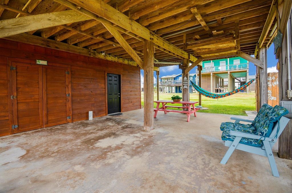 This outdoor space features a covered patio with wooden beams, a colorful hammock, and a picnic table, providing a cozy area for relaxation. 
