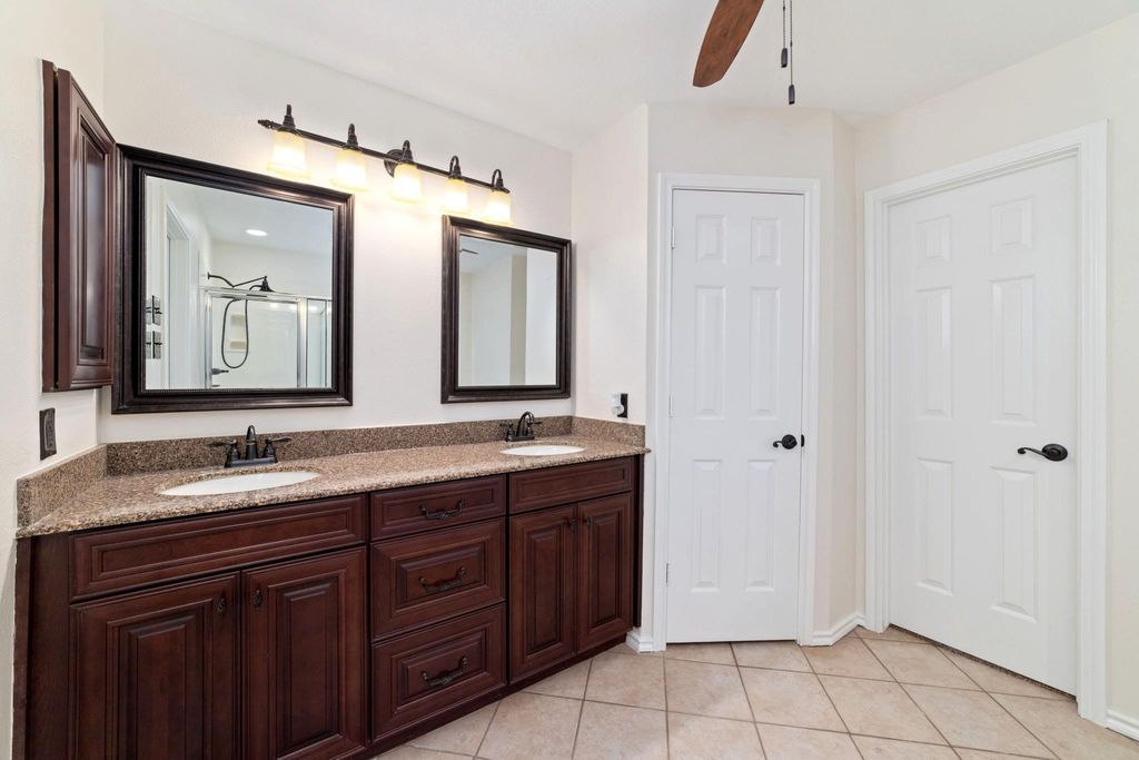 Open and airy primary bathroom featuring a double vanity with sleek quartz countertops, rich cherrywood finishes.