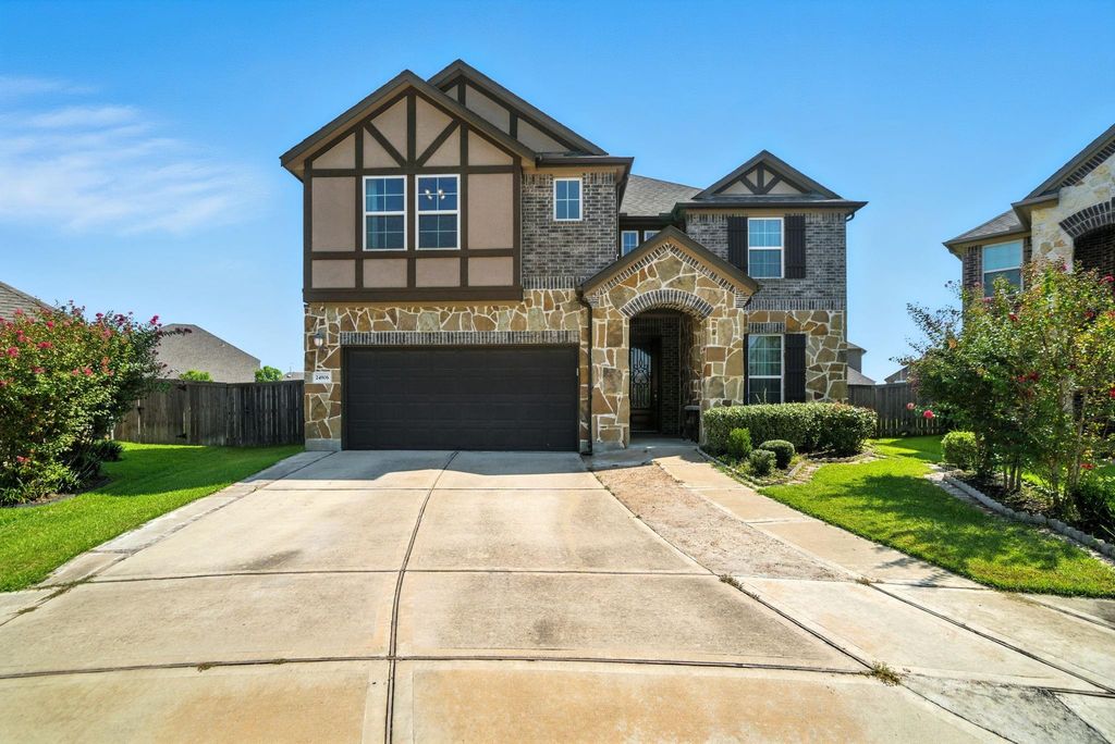 This charming two-story home features a mix of brick and stone exterior, a spacious driveway leading to a two-car garage, and a welcoming arched entryway. The well-maintained landscaping adds to its curb appeal.