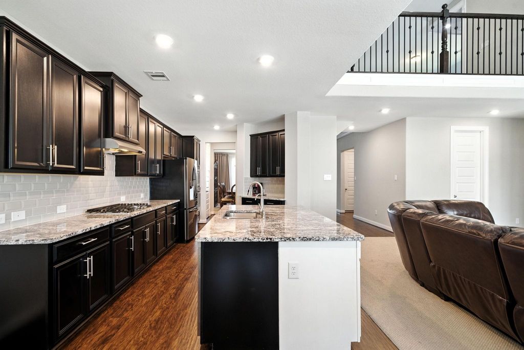 The open floor plan flows into a spacious living area with high ceilings and a view of the upstairs balcony.