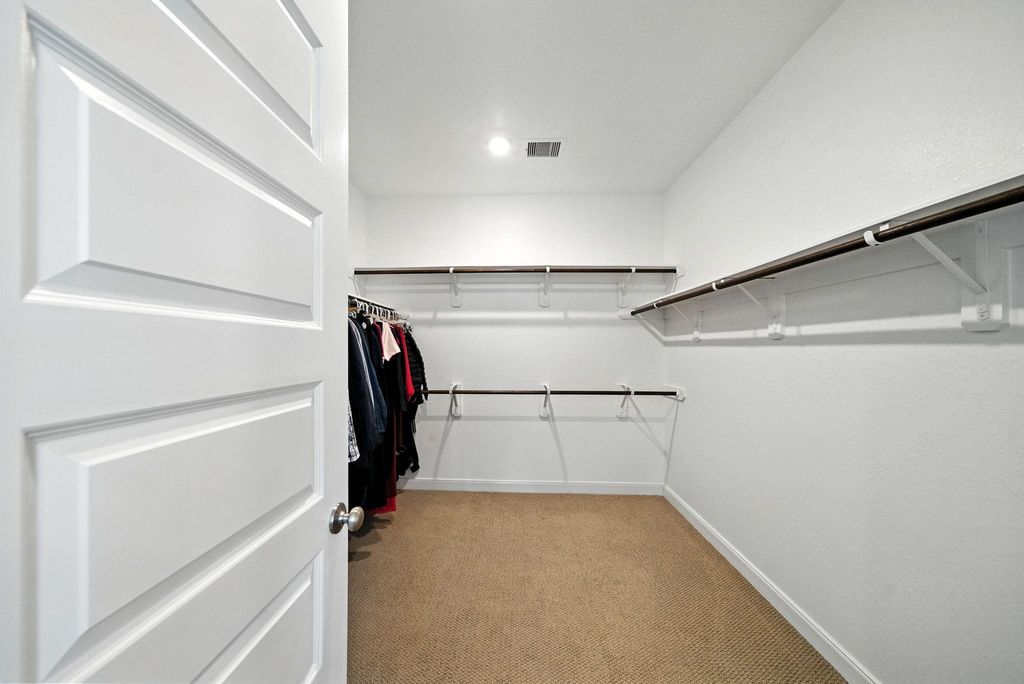 Spacious walk-in closet with ample hanging space, neutral carpeting, and bright white walls. Ideal for organizing clothes and accessories.