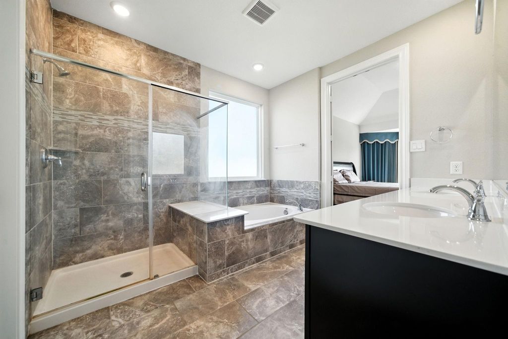 This modern bathroom features a spacious glass-enclosed shower, a luxurious soaking tub, and a dual-sink vanity with sleek fixtures. The neutral-toned tiles create a sophisticated atmosphere.