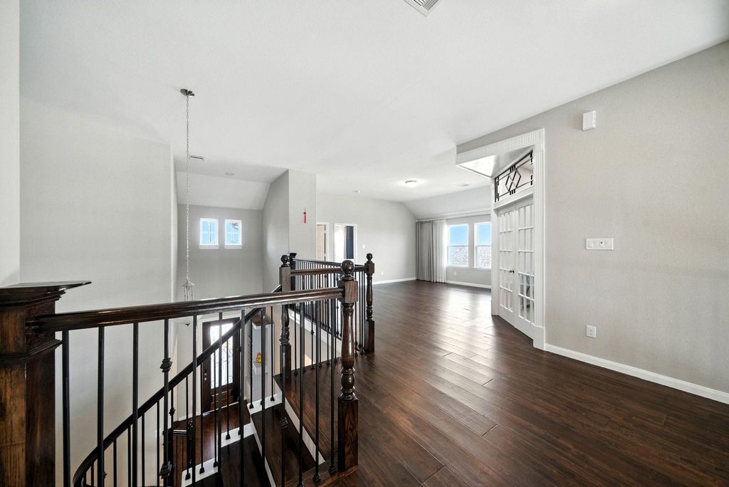 Bright and spacious upper landing area with elegant dark wood flooring and railings, featuring large windows and French doors leading to an additional room, perfect for a home office or sitting area.