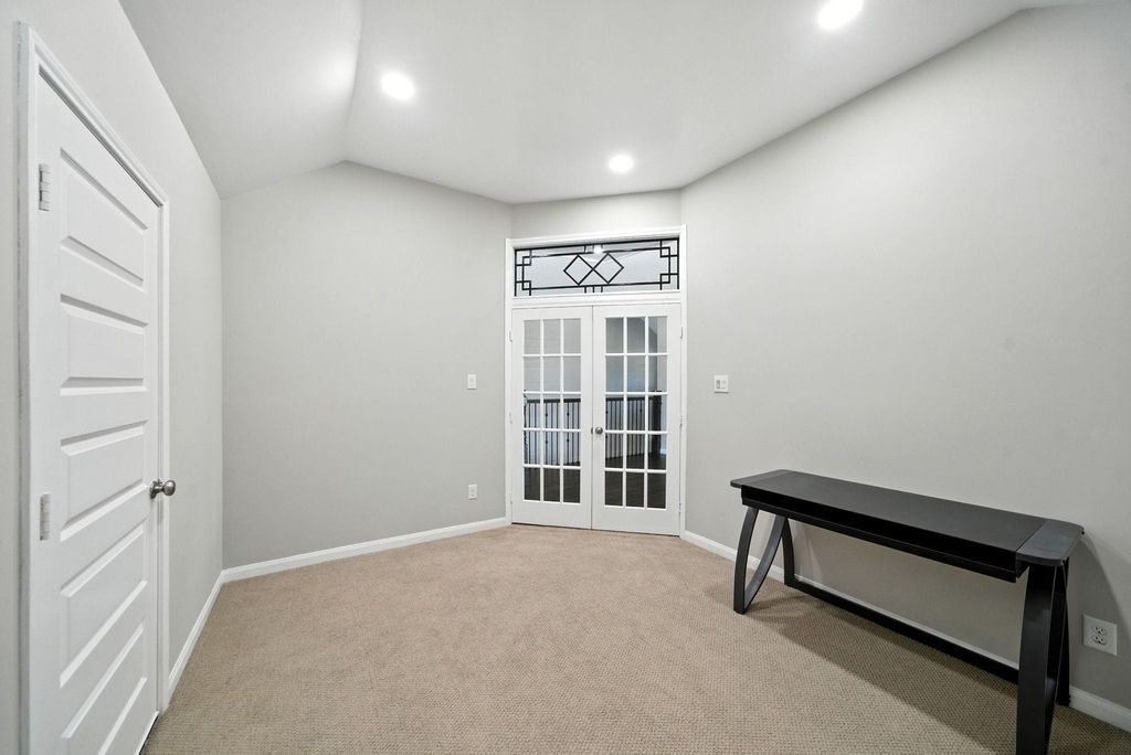 A neutral color palette with carpeted flooring, recessed lighting, and elegant French doors with decorative glass panels, creating a bright and versatile space.