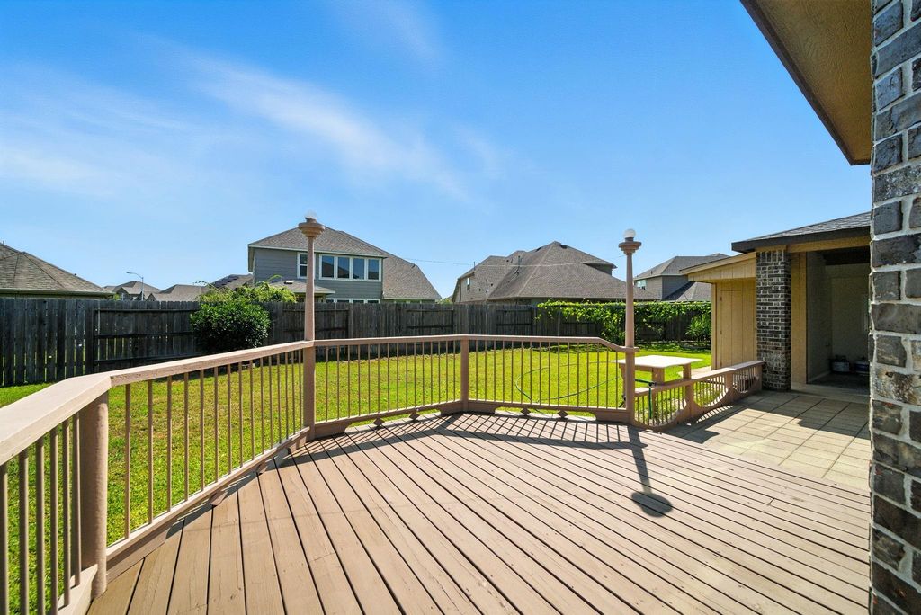 A spacious backyard featuring a deck with railings, perfect for outdoor gatherings. The yard is enclosed by a wooden fence, providing privacy. The area is well-maintained, offering ample space for gardening or recreation.